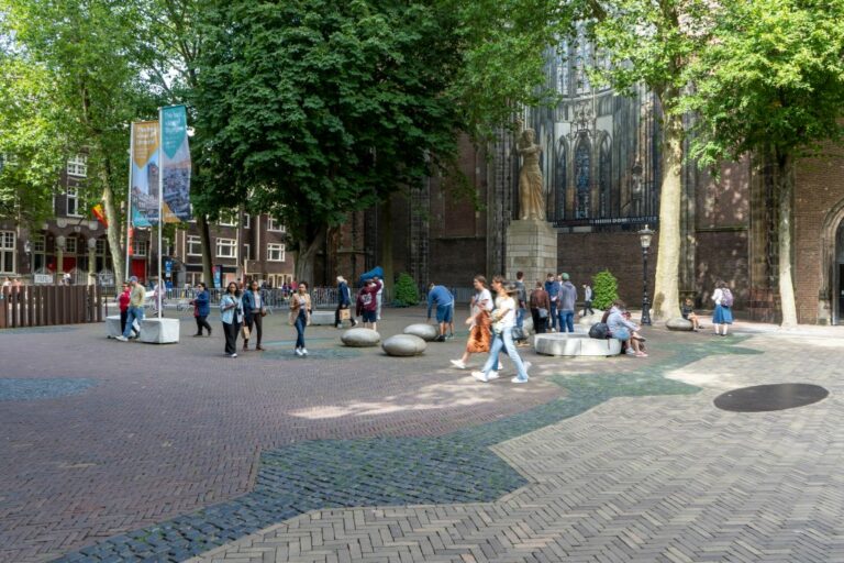 Platz vor einer Backsteinkirche in den Niederlanden, hohe Bäume, Leute, Denkmal