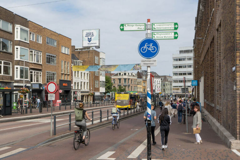 Radfahrer fahren auf einem Radweg neben einer Bushaltestelle vorbei