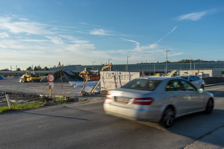 Auto fährt an einer Baustelle vorbei, Plakat "Lobau bleibt"