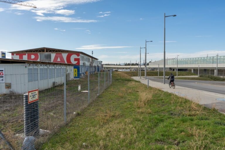 Baustellencontainer und Zaun neben einer U-Bahn-Station, Laternenmasten, Radfahrer, Grünfläche