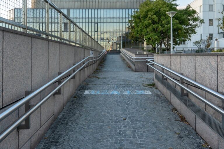 Fußweg mit Geländern auf beiden Seiten, Gebäude mit Glasfassade, Bäume