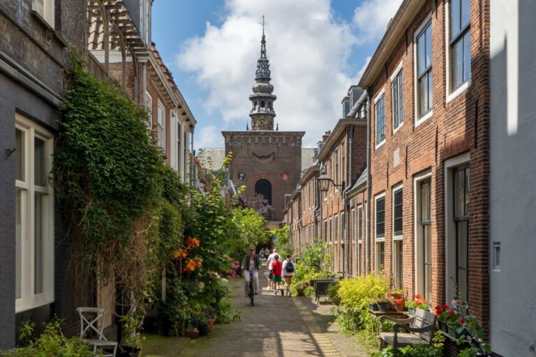 Leute und Radfahrerin in einer Gasse mit vielen Pflanzen, Kirche