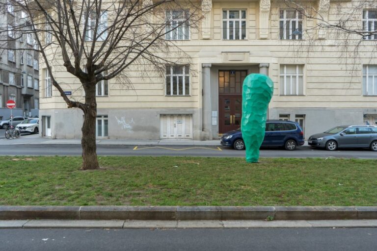 Skulptur von Franz West auf einer Grünfläche neben einem Baum, dahinter ein Gründerzeithaus