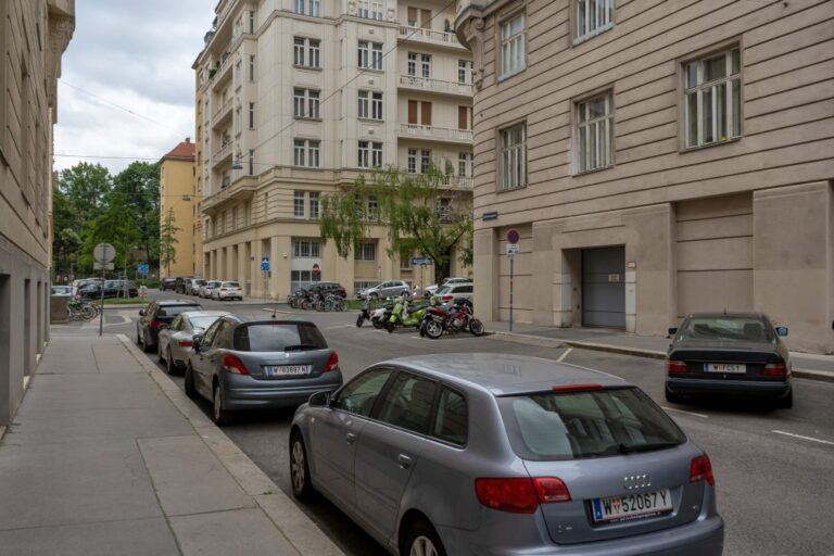 Gasse neben einem Platz mit hohen Altbauten und parkenden Autos